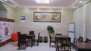 A dining area with a table and chairs, a painting on the wall, a potted plant, and a refrigerator. - Jinmalou Hotel (Yueqing)