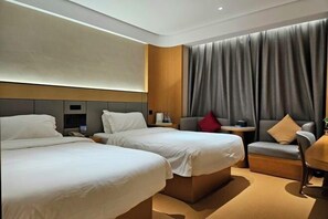 Une chambre d’hôtel avec deux lits, une petite table, un canapé et une grande fenêtre avec des rideaux.