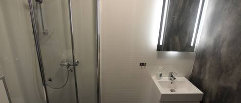 A bathroom with a glass-enclosed shower, a white sink with a mirror above it, and a dark tiled floor.