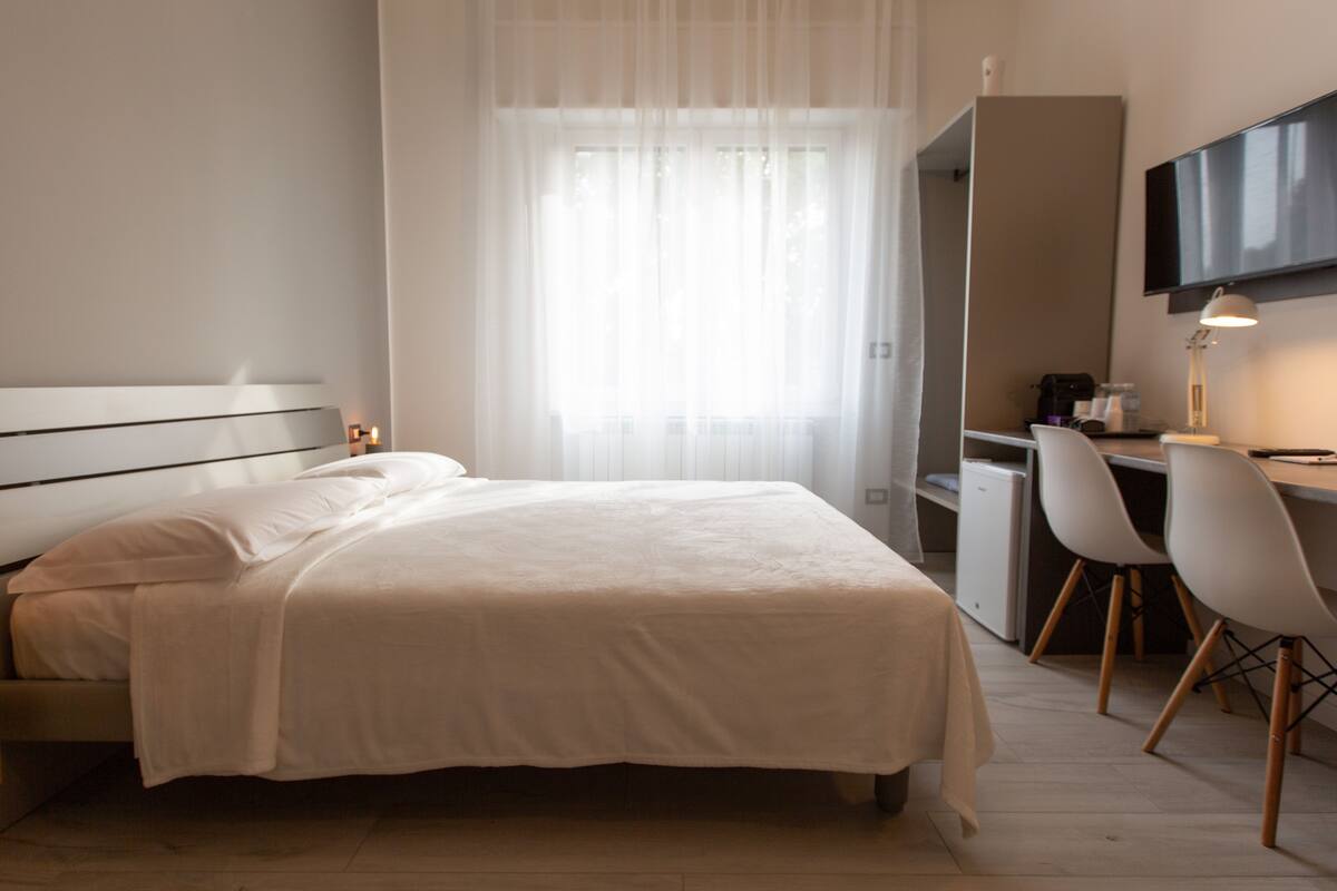 Een hotelkamer met een bed, een bureau met stoel, een televisie en een raam met gordijnen.