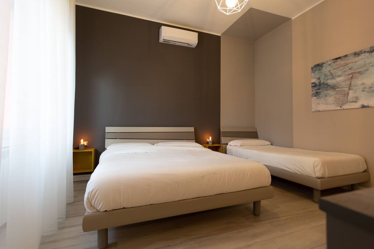 Een moderne slaapkamer met twee enkele bedden, een nachtkastje met een lamp en een wandairconditioner.