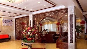 Eine Hotellobby mit einer Rezeption, einem dekorativen Bogen, einem roten Teppich und einer großen Blumenkomposition.