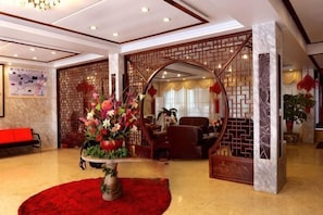 A hotel lobby with a reception desk, a decorative archway, a red carpet, and a large floral arrangement. - Mingyan Hotel (Yueqing)