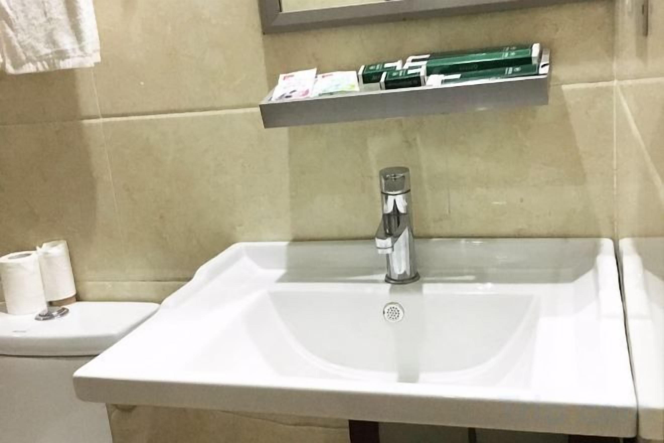 A bathroom with a white sink, a mirror, and a shelf above the sink.