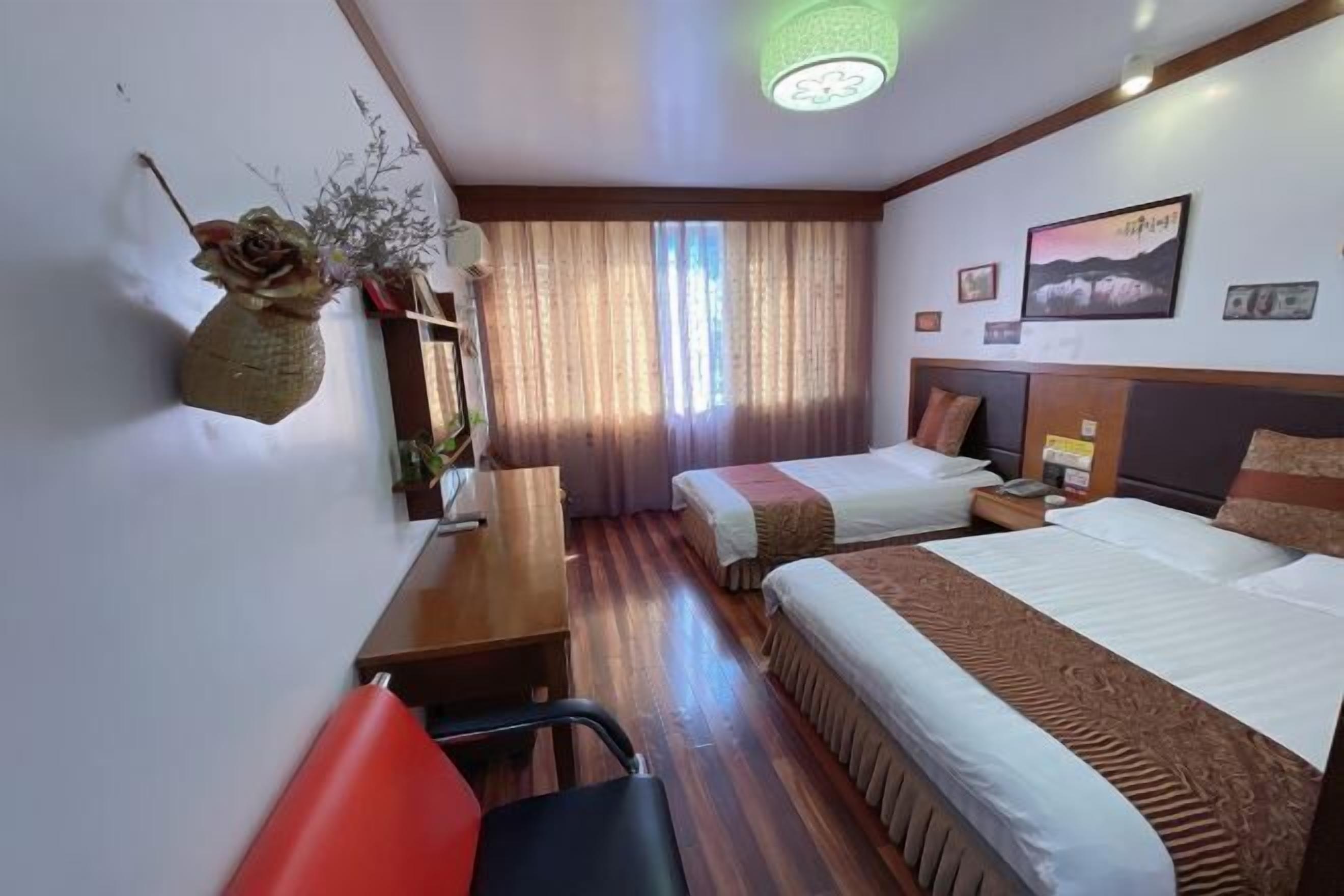 Ein Hotelzimmer mit zwei Betten, einem Schreibtisch, einem Stuhl, einem Fenster mit Vorhängen und einer Wand-Klimaanlage.