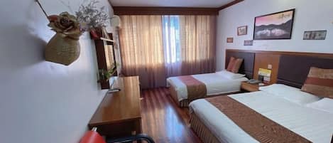 A hotel room with two beds, a desk, a chair, a window with curtains, and a wall-mounted air conditioner.