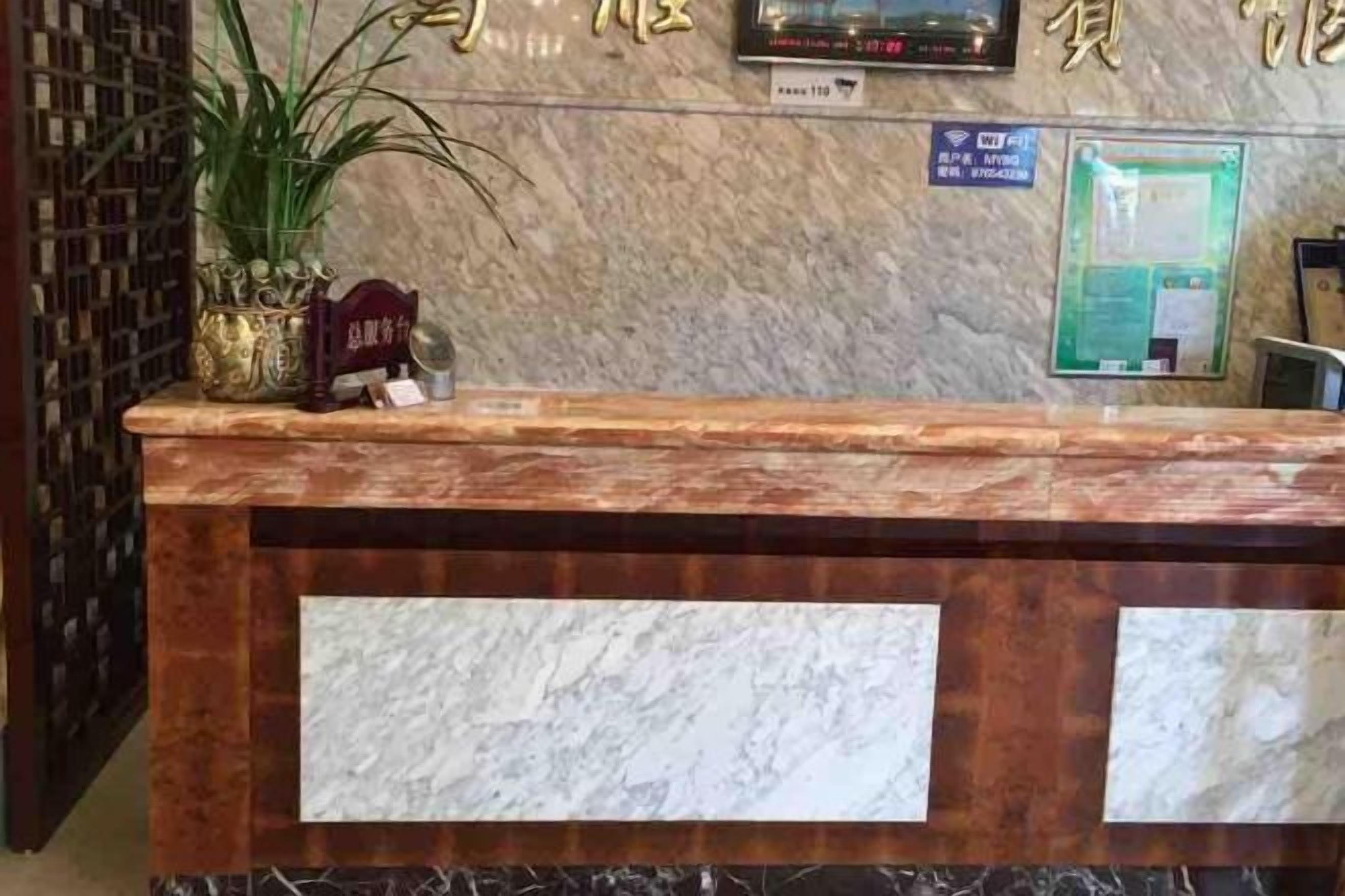 A reception desk with a marble top, a potted plant, and a sign above indicating the hotel's name.