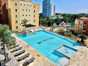 A swimming pool with a pergola, lounge chairs, and a view of a marina and high-rise buildings.