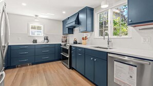 A modern kitchen with dark blue cabinets, a stainless steel refrigerator, a built-in oven, and a window providing natural light. - Minutes to Nauset Beach, Central AC, Game Space! (Orleans)