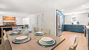 A modern kitchen with a dining area, featuring a wooden table set for four, a refrigerator, and blue cabinets. - Minutes to Nauset Beach, Central AC, Game Space! (Orleans)