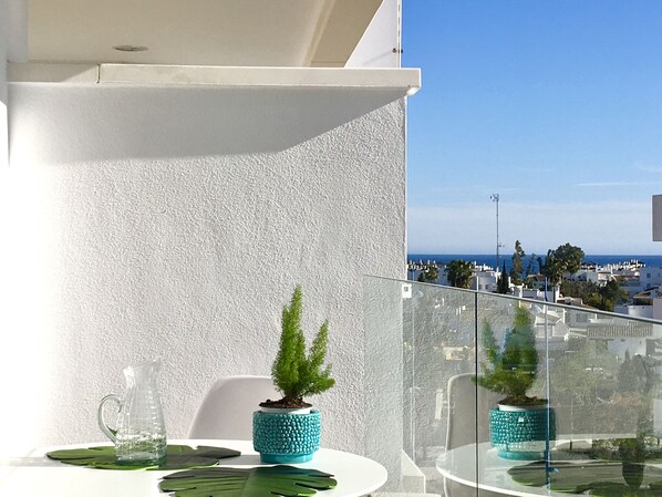 A balcony with a white textured wall, a glass table, and a small potted plant. - Marbella Beachside Penthouse (San Pedro Alcántara)