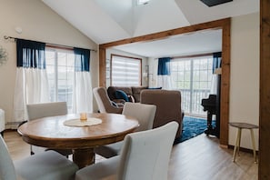 Una sala de estar acogedora con una mesa redonda de madera, asientos cómodos y ventanas amplias con cortinas.
