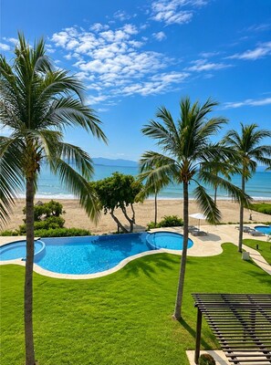A pool area with a curved design, surrounded by palm trees and a view of the beach. - Punta Mita Beachfront 5 Star Luxury (Punta de Mita)