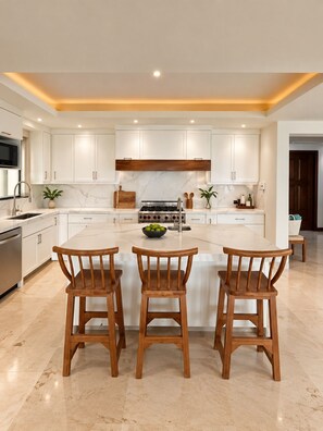 Una cocina moderna con armarios blancos, una isla central con taburetes y una campana extractora de acero inoxidable.