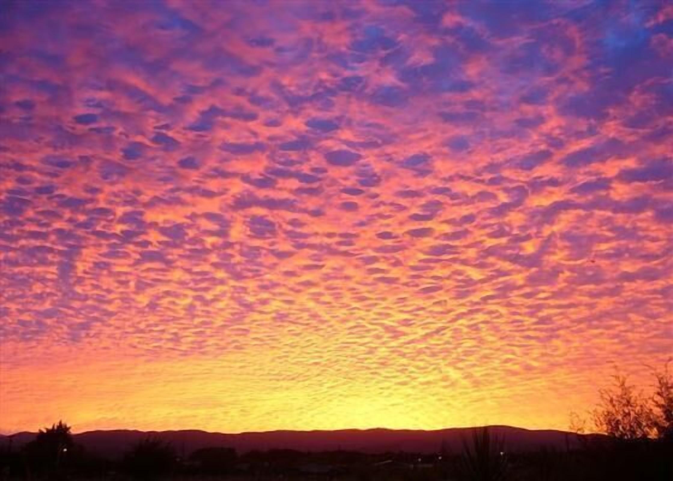 A sunset with a clear sky and silhouettes of distant hills.