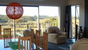 A room with a dining table, chairs, a sofa, and a large window offering a view of a landscape. - Waterviews and relaxation (Paihia)