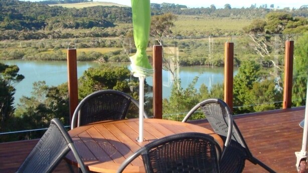 A wooden deck with a round table and four chairs, overlooking a lake and hilly landscape. - Waterviews and relaxation (Paihia)