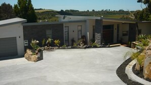 A modern house with a garage, a driveway, and a landscaped garden with rocks and plants. - Waterviews and relaxation (Paihia)