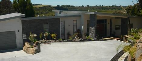 Ein modernes Haus mit Garage, Auffahrt und einem angelegten Garten mit Steinen und Pflanzen.