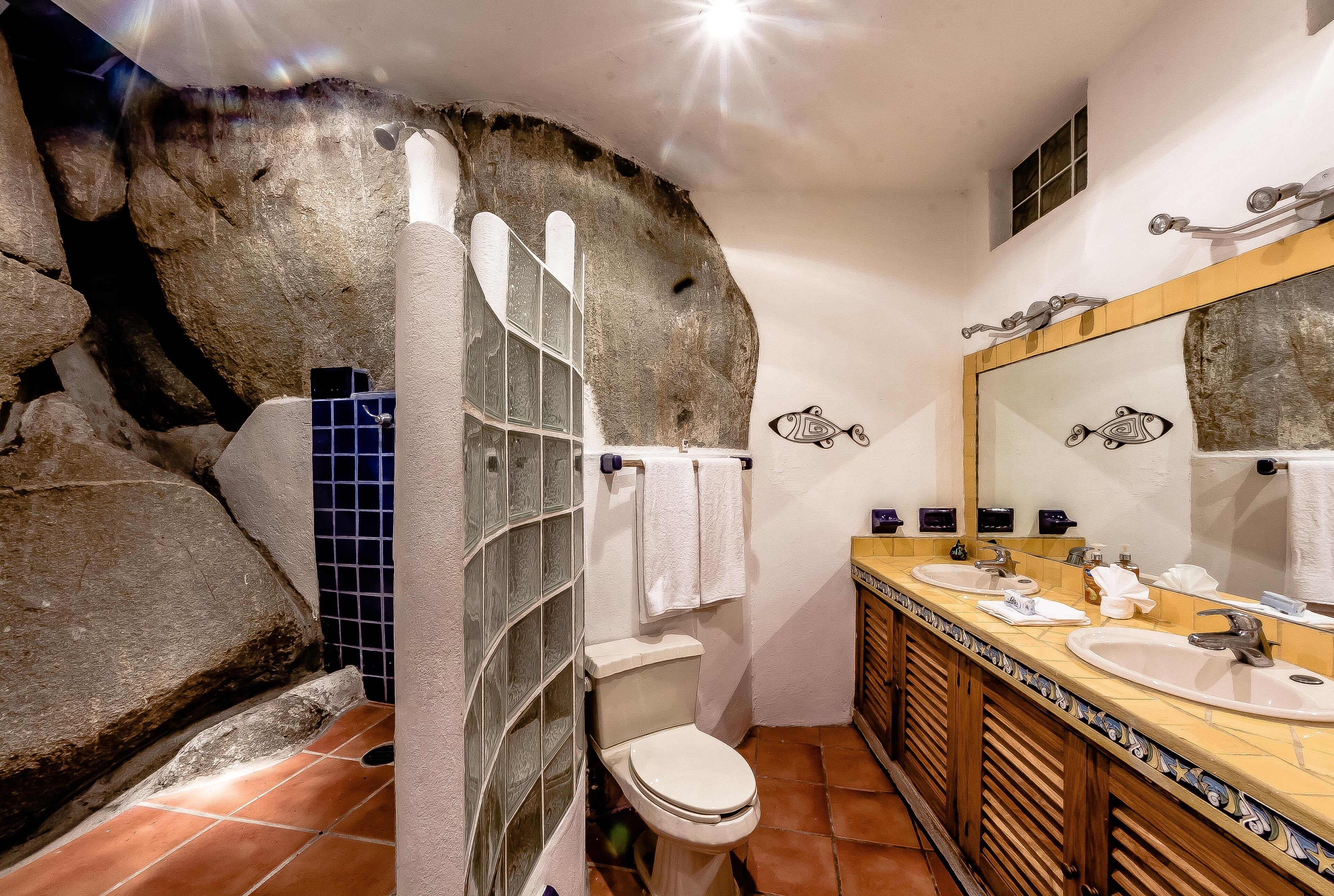 Une salle de bain avec un mur en pierre rustique, une cabine de douche en verre et un meuble-lavabo en bois doté de deux vasques.