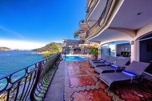 Zona junto a la piscina con sillones de descanso, piscina y vista al mar.