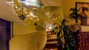 A staircase with a curved wall, star-shaped hanging lights, a potted plant, and a decorative wooden panel.