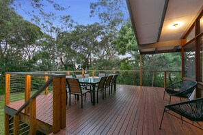 An outdoor deck with a table and chairs, surrounded by a wooden railing and overlooking a forested area.