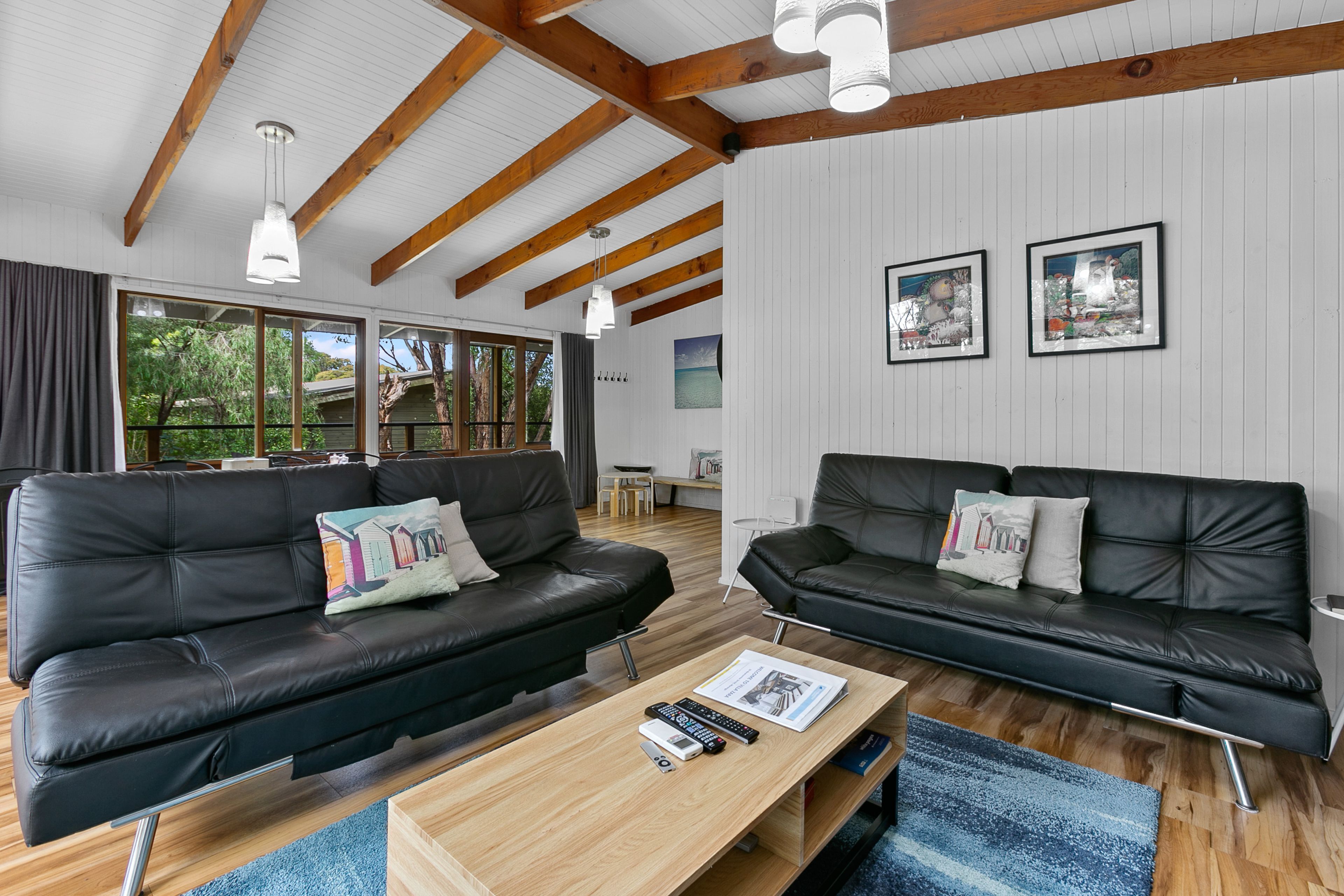 Una sala de estar moderna con dos sofás de cuero negro, una mesa de centro de madera y vistas al exterior a través de amplios ventanales.