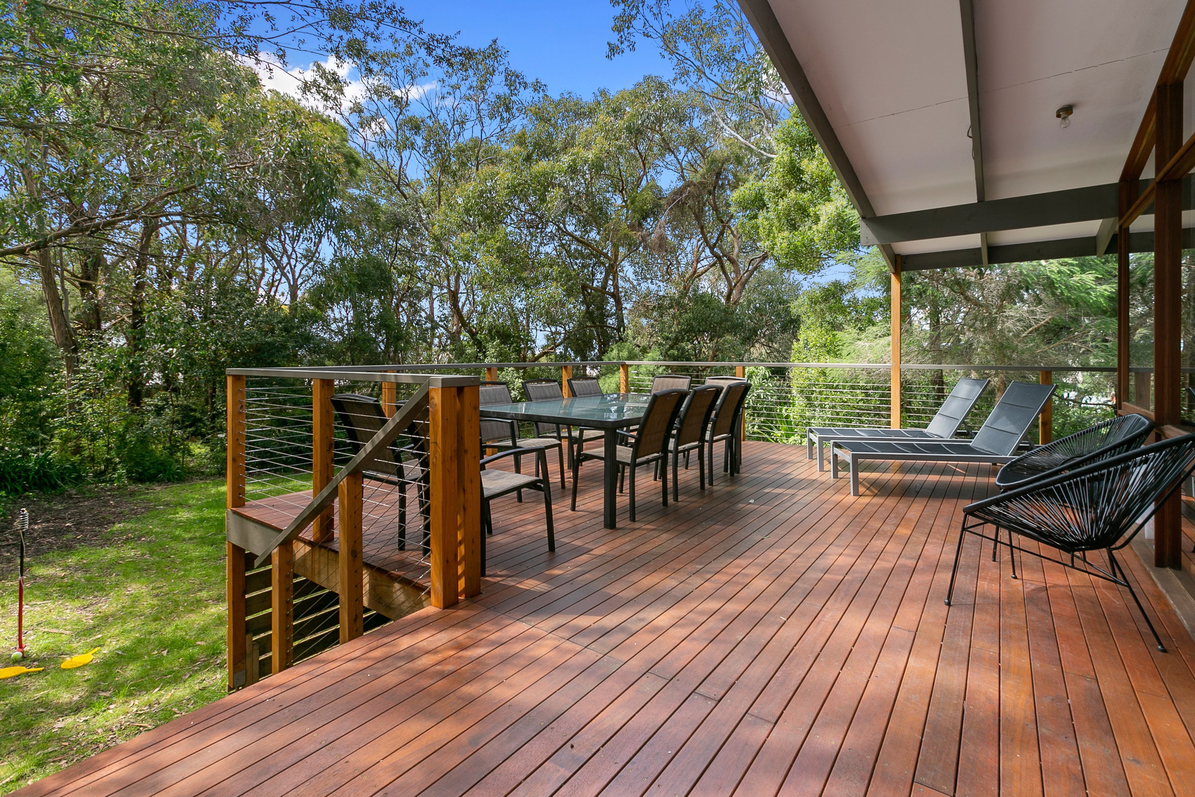 Une terrasse en bois, aménagée avec du mobilier d’extérieur, notamment une table et des chaises, et une zone couverte dotée d’une rambarde.