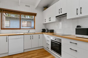 Eine moderne Küche mit weißen Schränken, einer Holz Arbeitsplatte, einem eingebauten Geschirrspüler, einem Herd und einer Mikrowelle.