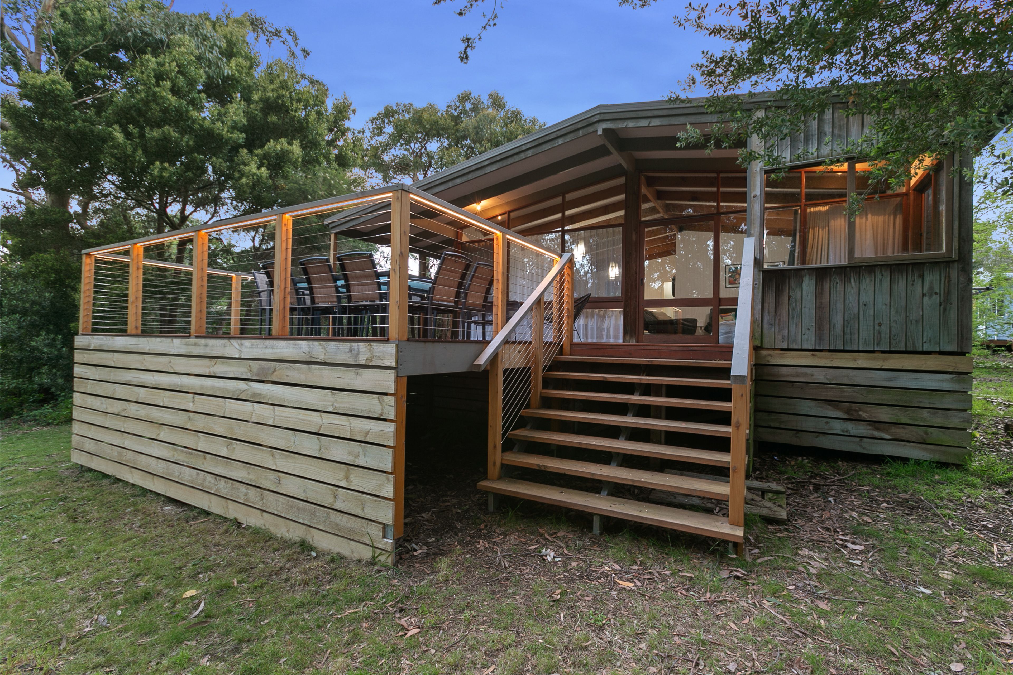 A wooden cabin with a covered outdoor seating area and a staircase leading to a loft.