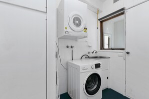 A compact laundry room with a front-loading washing machine, a sink, and a mirror above the mirror.