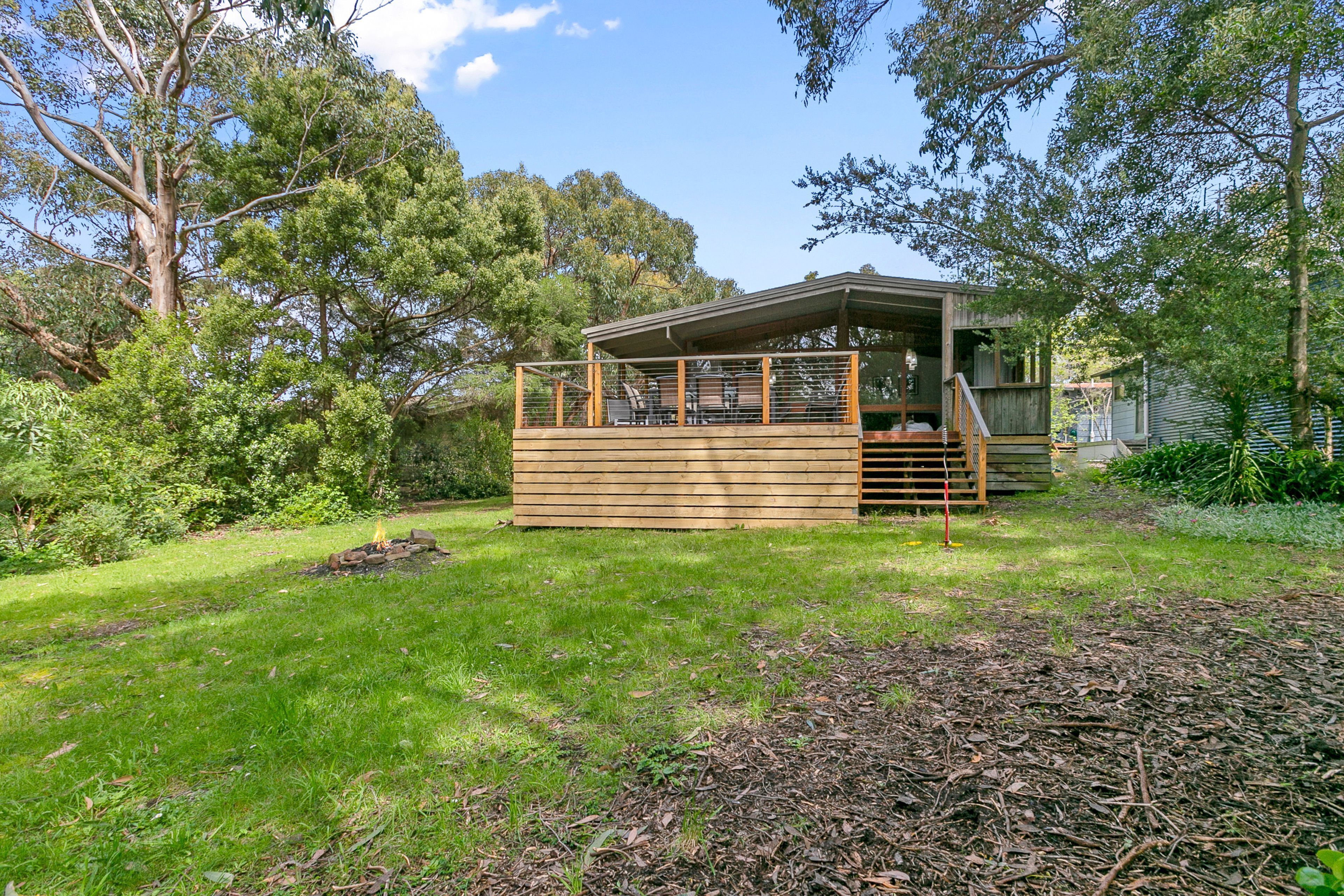A wooden cabin with a deck, surrounded by lush greenery and trees.