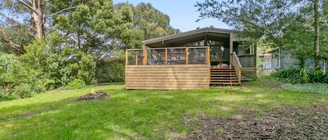 A wooden cabin with a deck, surrounded by lush greenery and trees.
