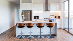 Een moderne keuken met witte kasten, een centraal eiland met barkrukken, een roestvrijstalen koelkast en een groot raam met uitzicht.