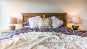 Een net opgemaakt bed met een bedsprei met een patroon, twee zachte kussens en twee bedlampjes op houten nachtkastjes.