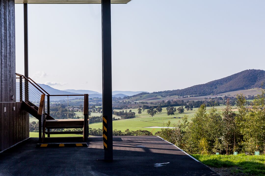 A covered outdoor area with a view of a green valley and hills.