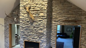 A stone fireplace with a mounted animal head, a wooden door, and a mirror reflecting a living room. - 🌲☀️Private Lakefront prop. with Kayaks, Paddle boards, boat rental PVT dock☀️🌲 (Twin Lakes)