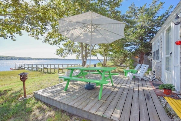 A wooden deck with picnic tables and an umbrella, overlooking a body of water. - Fish or boat directly off our shared dock! (Eastham)