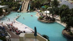 Een zwembadgedeelte van een resort met een centrale glijbaan, verschillende zwemgedeeltes en ligbedden.