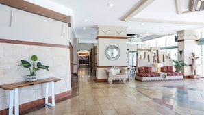 Un vestíbulo espacioso con una recepción, un espejo decorativo y una zona de estar con cojines estampados.