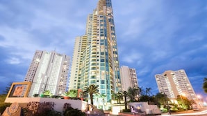 Un edificio alto y moderno con múltiples balcones, rodeado de palmeras y otra vegetación.
