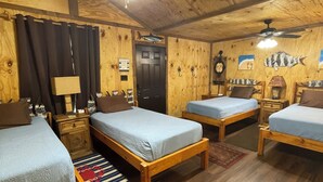 Ein Blockhaus-Zimmer mit drei Holzbetten und Wandlüfter, die Wände sind aus Holz.