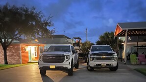Eine Auffahrt mit zwei weißen Pick-up-Trucks, ein kleines Gebäude mit beleuchtetem Eingang und einem klaren Himmel.