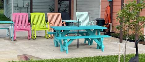A covered patio area with colorful Adirondack chairs and picnic tables.