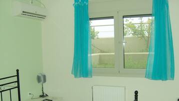 A room with a bed, an air conditioner, a window with curtains, a bedside table with a lamp, and a radiator.