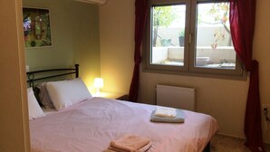 Ein Schlafzimmer mit einem Bett, einem Nachttisch, einer Lampe, einer Klimaanlage, einem Fenster mit Vorhängen und einem Heizkörper.