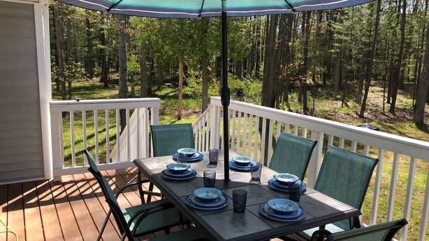 Une terrasse avec une table dressée pour quatre personnes, entourée de chaises, sous un parasol à rayures.