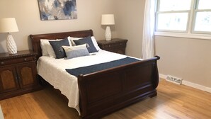 Une chambre à coucher avec un lit en bois, du linge de lit blanc, deux tables de chevet avec des lampes et une fenêtre avec des rideaux.