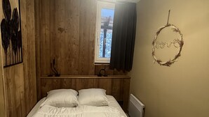 A bedroom with a wooden headboard, a bed with white bedding, a ceiling light fixture, a window with curtains, and a wall decoration with the word "love". - Resort center, app. 36 m2, 1 bedroom, mountain corner, balcony, ski room, WIFI (Morzine)